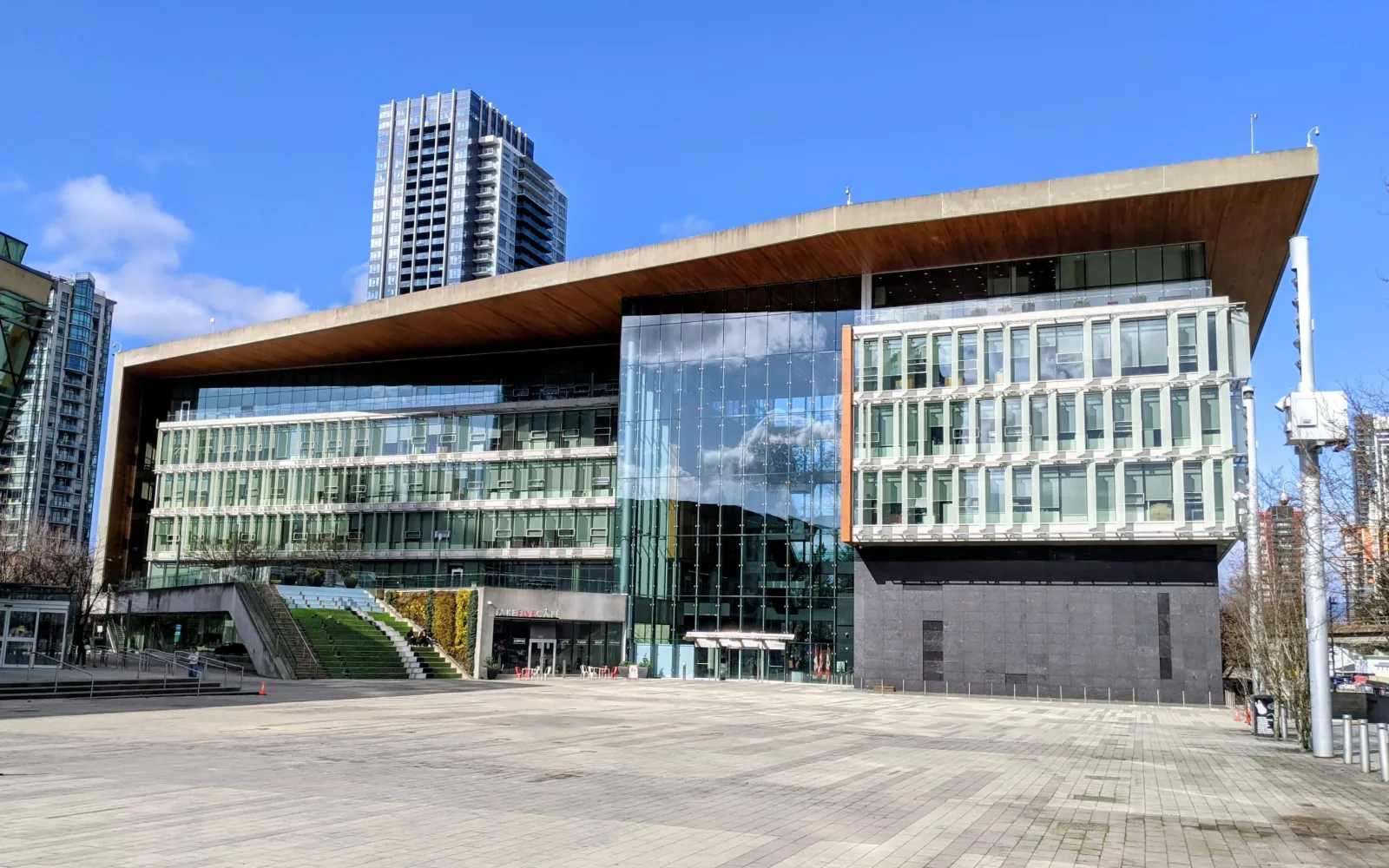 Surrey City Hall, a glass and stone building under a wide wooden roof, across an empty paved plaza under a blue sky