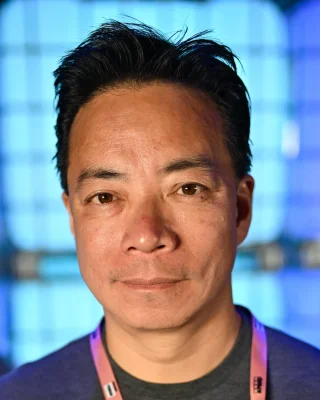 Portrait of Ken Sim at Collision 2024, with a blue background.